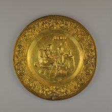 Mosazný nástěnný talíř s reliéfem babky a dědka hrajícího na hou